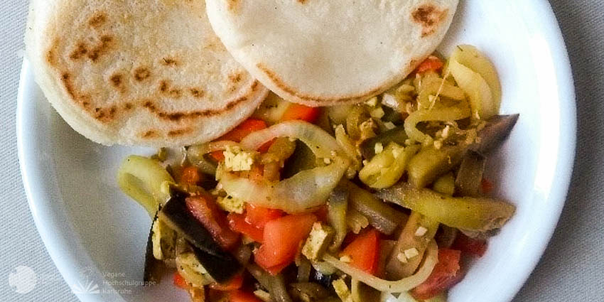Zwei Arepas (traditionelle Maisfladen aus Venezuela) liegen neben buntem Gemüse auf einem weißen Teller.