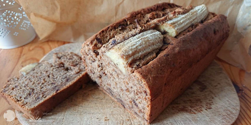 Ein angeschnittenes Brot auf einem Brett auf dessen Oberseite halbierte Bananen sind