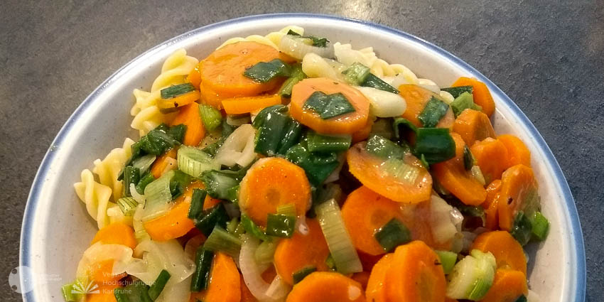 Karotten, Frühlingszwiebeln, Nudeln mit Öl übergossen, auf einem Teller.