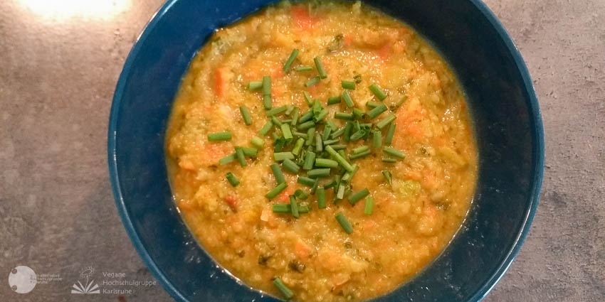 In einer blauen Schüssel, ist eine goldgelbe Suppe, mit Schnittlauch überstreut.