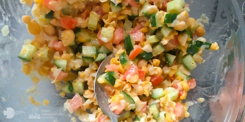 Gurken, Tomaten, Mais und Kichererbsen in einer Glasschüssel mit Dressing überzogen.