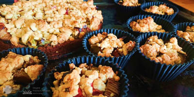 Ein großer Streuselkuchen und im Vordergrund viele kleinere in blauen Muffinformen.
