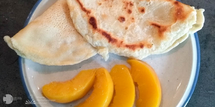Auf dem Teller liegen zwei zusammengeklappte Pfannkuchen daneben vier Pfirsichspalten.